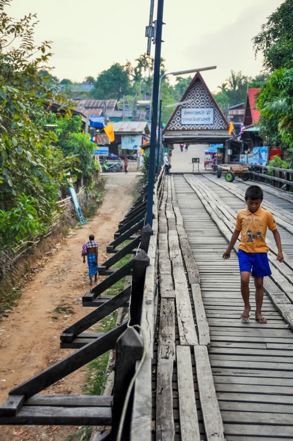 Garçon traversant un pont en bois dans un village thaïlandais