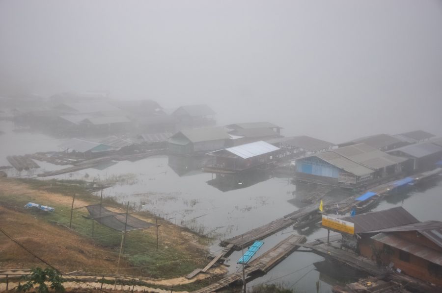 Village lacustre brumeux avec maisons sur pilotis et bateaux