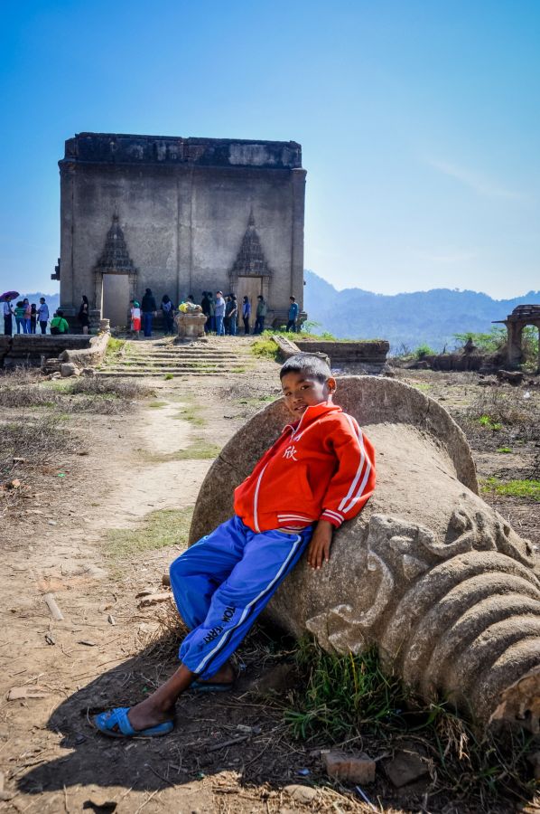 Garçon assis devant un temple ancien entouré de visiteurs