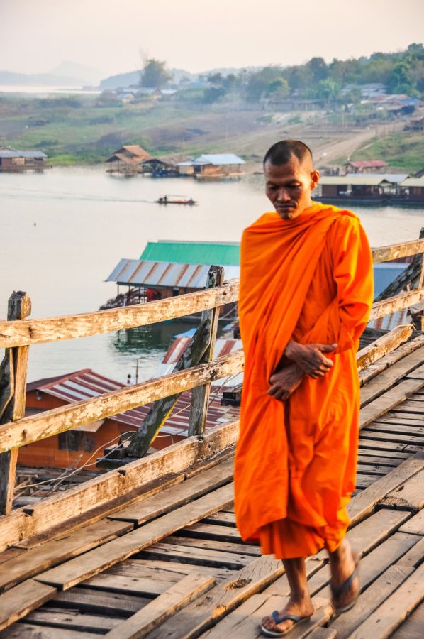 Moine bouddhiste en robe orange sur un pont en bois