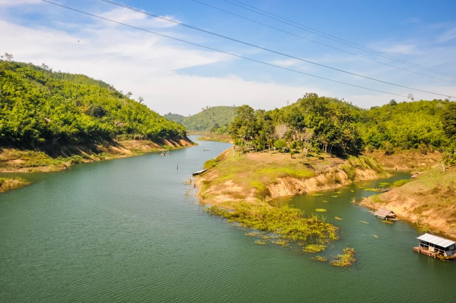 Lac sinueux entouré de collines boisées et cabanes flottantes