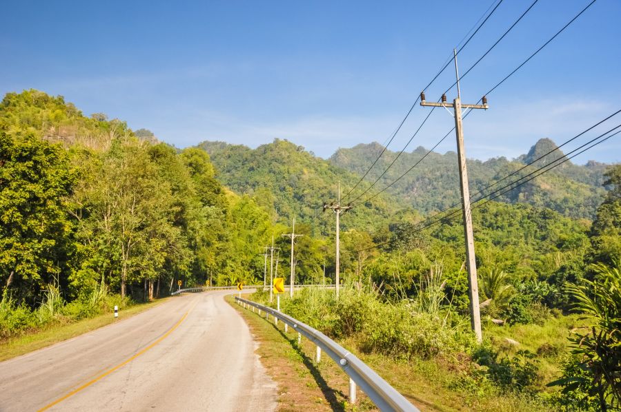 Route sinueuse dans une forêt tropicale avec poteaux électriques