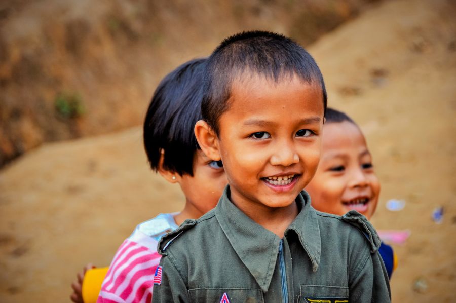 Trois enfants souriants devant un mur en terre
