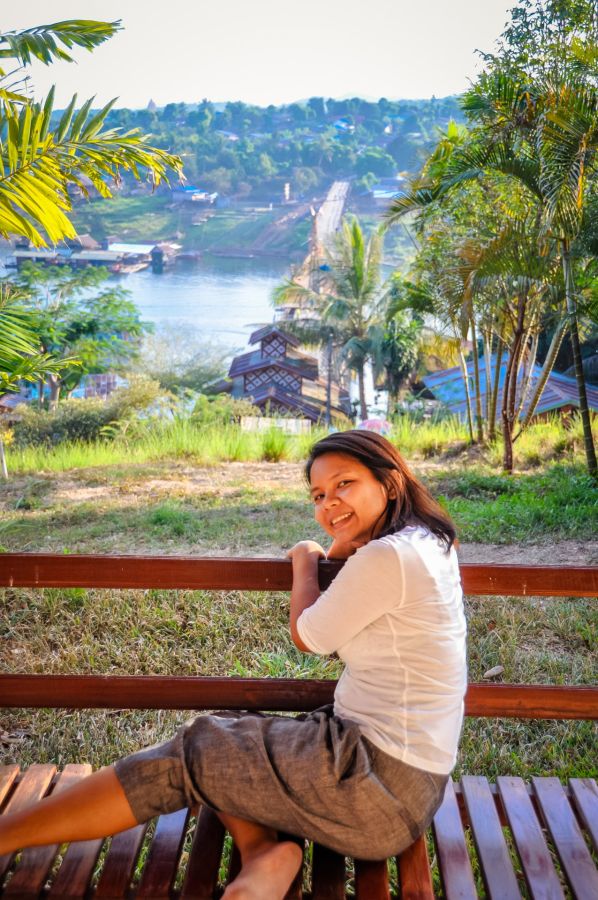 Femme souriante sur un banc devant une rivière tropicale