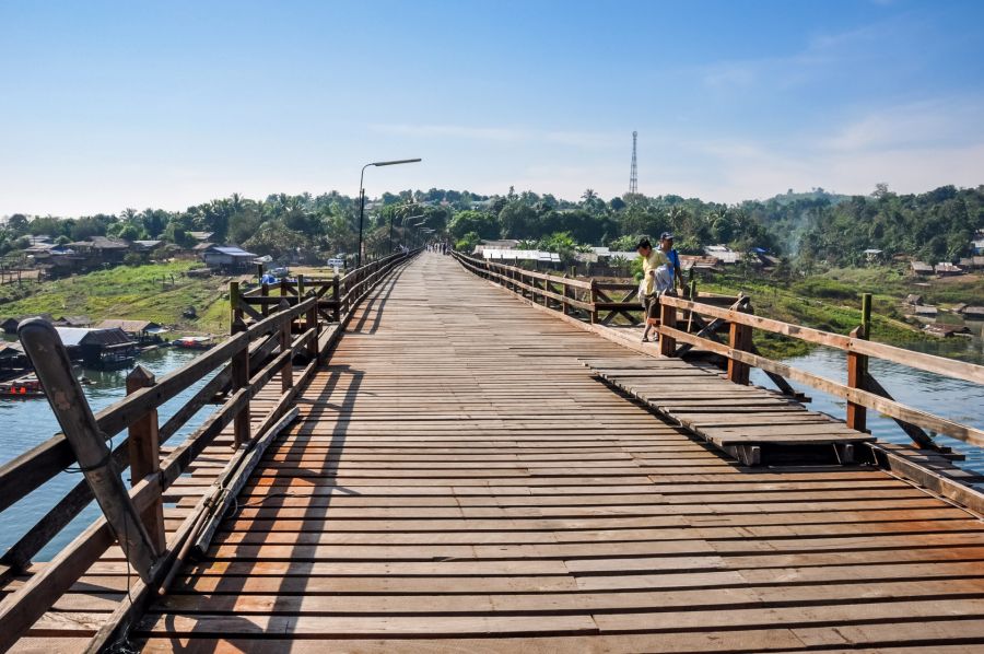 Pont en bois traversant une rivière vers un village tropical