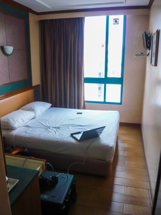 Chambre d’hôtel étroite avec lit, ordinateur portable et fenêtre
