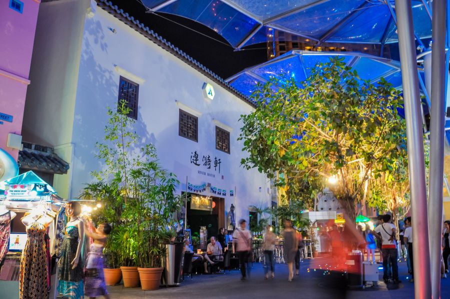 Rue nocturne animée avec restaurants, boutiques et verrière bleue