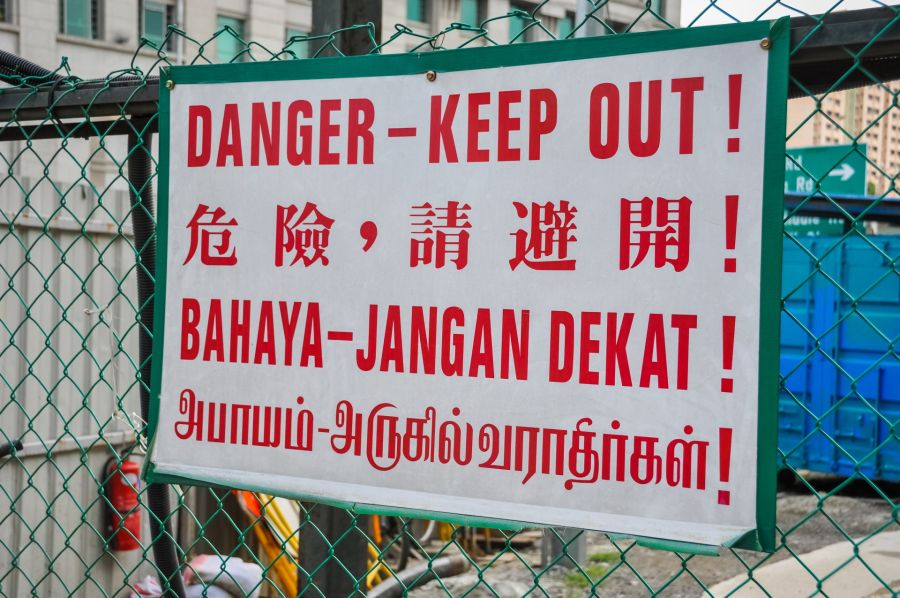 Panneau multilingue « Danger, accès interdit » sur grille de chantier