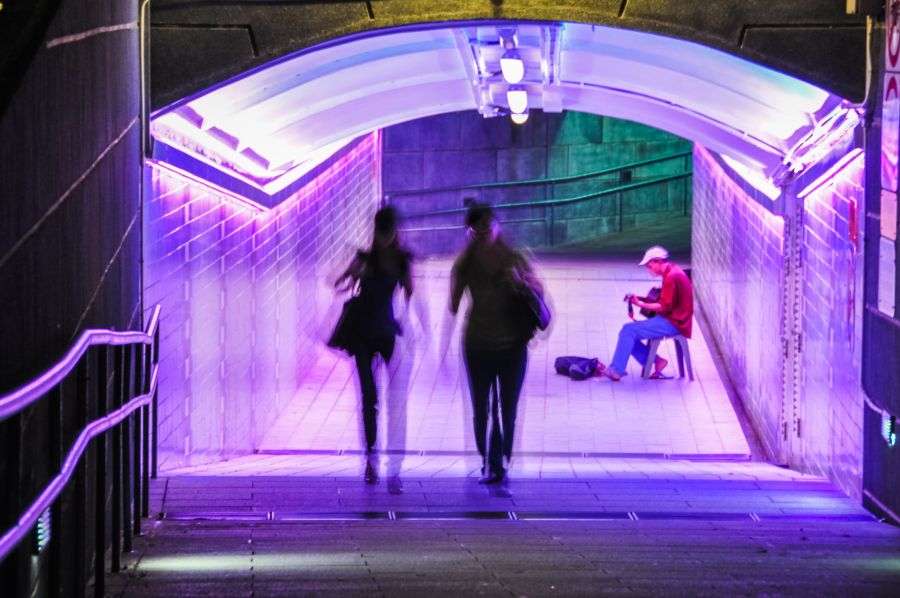 Couloir de métro violet avec passants et musicien assis