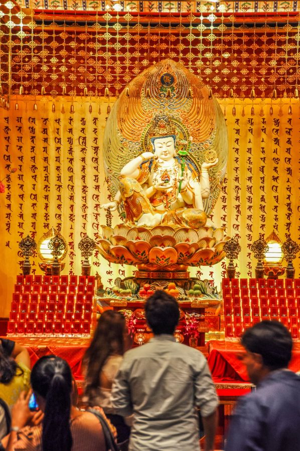 Statue bouddhiste dorée devant fidèles dans un temple orné