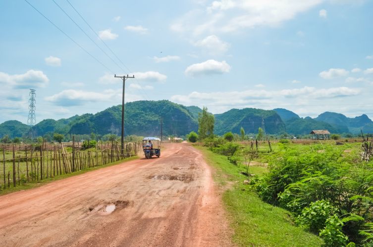 Tuk-tuk sur route rurale, montagnes verdoyantes au loin