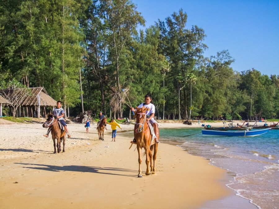 Enfants à cheval sur une plage près de bateaux