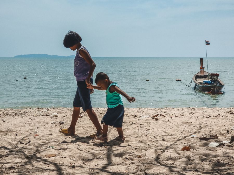 Deux enfants marchent main dans la main sur une plage.
