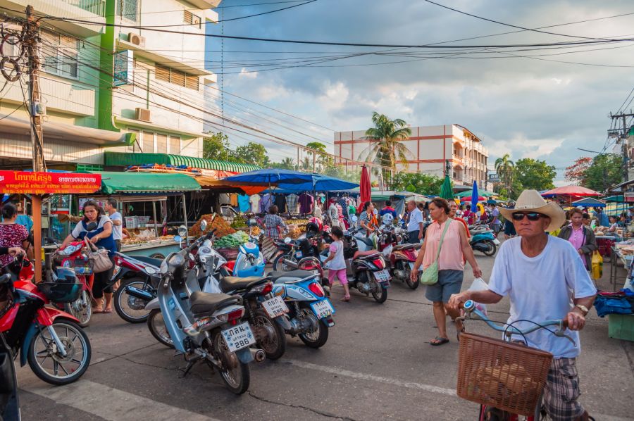 Marché thaïlandais animé avec scooters, étals et passants