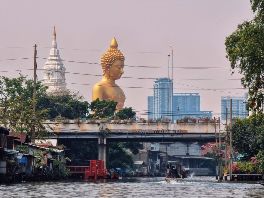 Grand Bouddha doré dominant canal urbain et temple blanc
