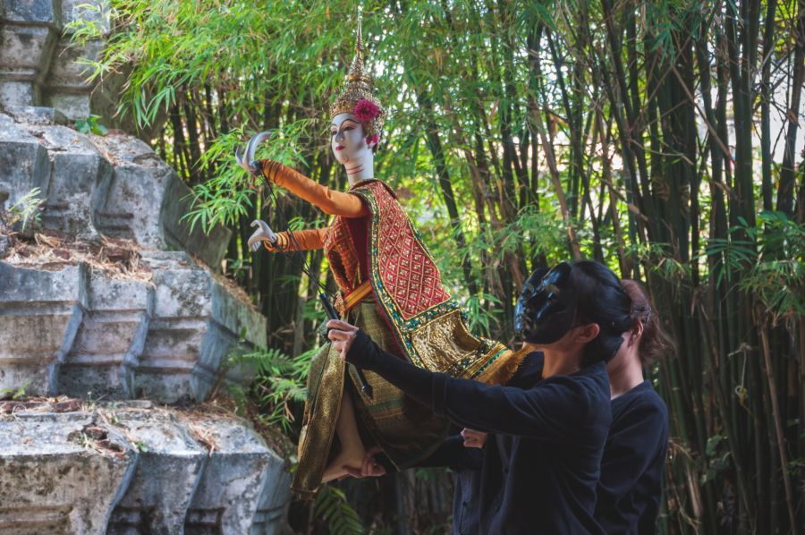 Marionnettistes manipulant une danseuse traditionnelle devant des bambous