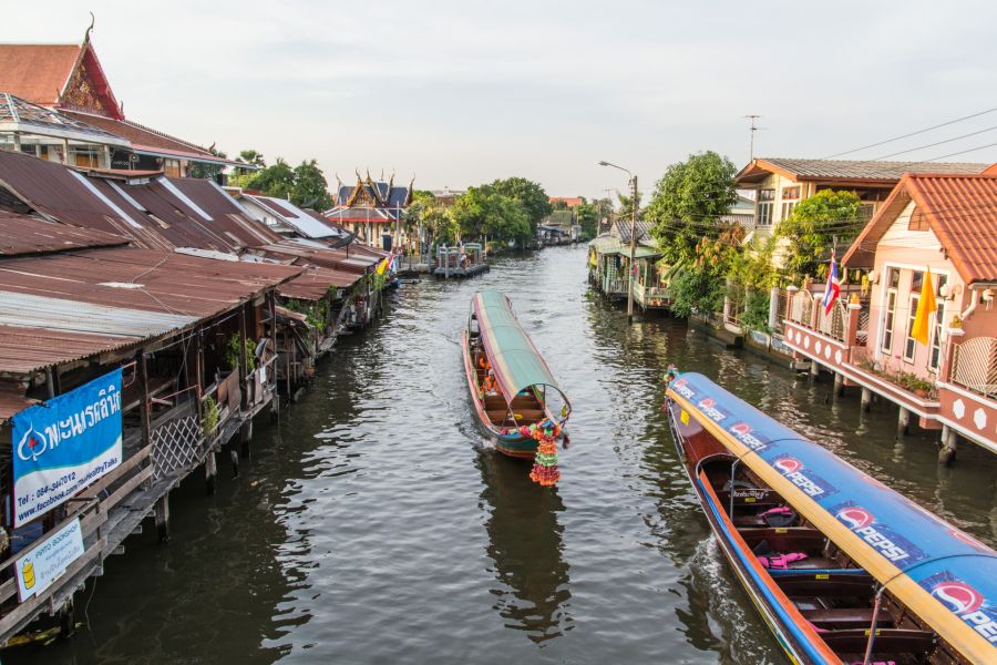 Pirogues naviguant sur un canal bordé de maisons thaïlandaises