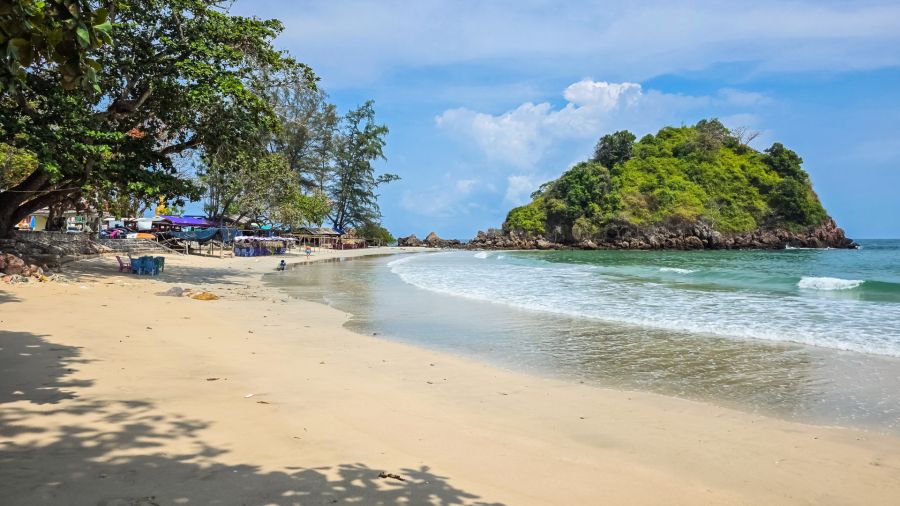 Tropical beach lined with trees, waves and a green rocky islet