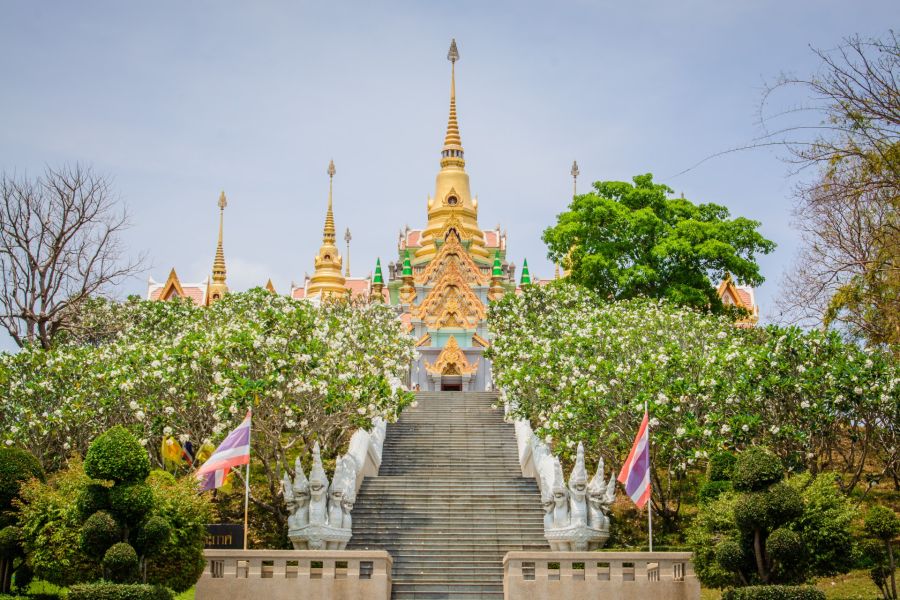 Golden Buddhist temple with staircase, statues and flower garden