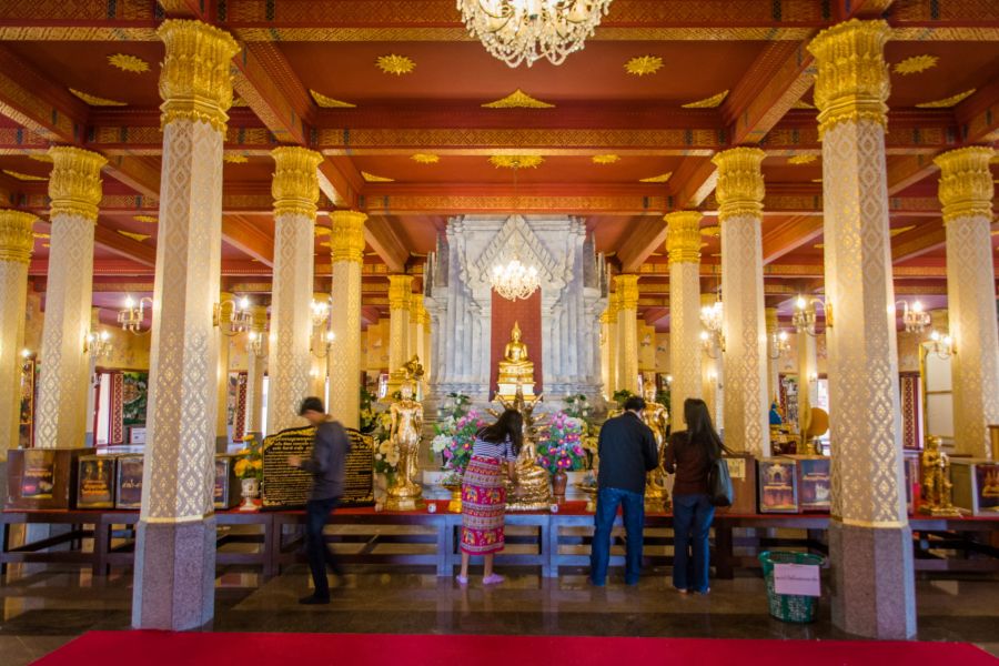 Worshippers praying before Buddha in an ornate Thai temple