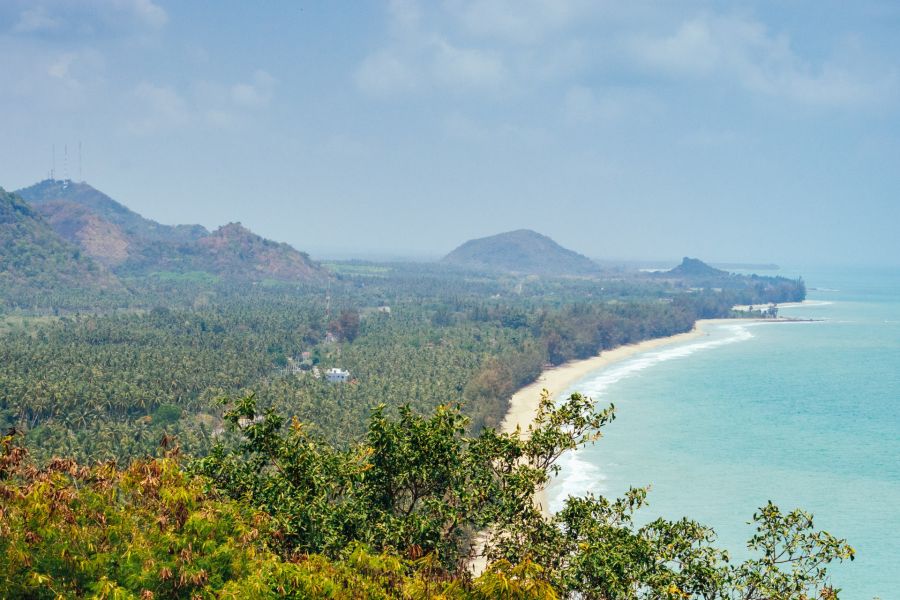 Tropical beach lined with palm trees, hills and turquoise sea