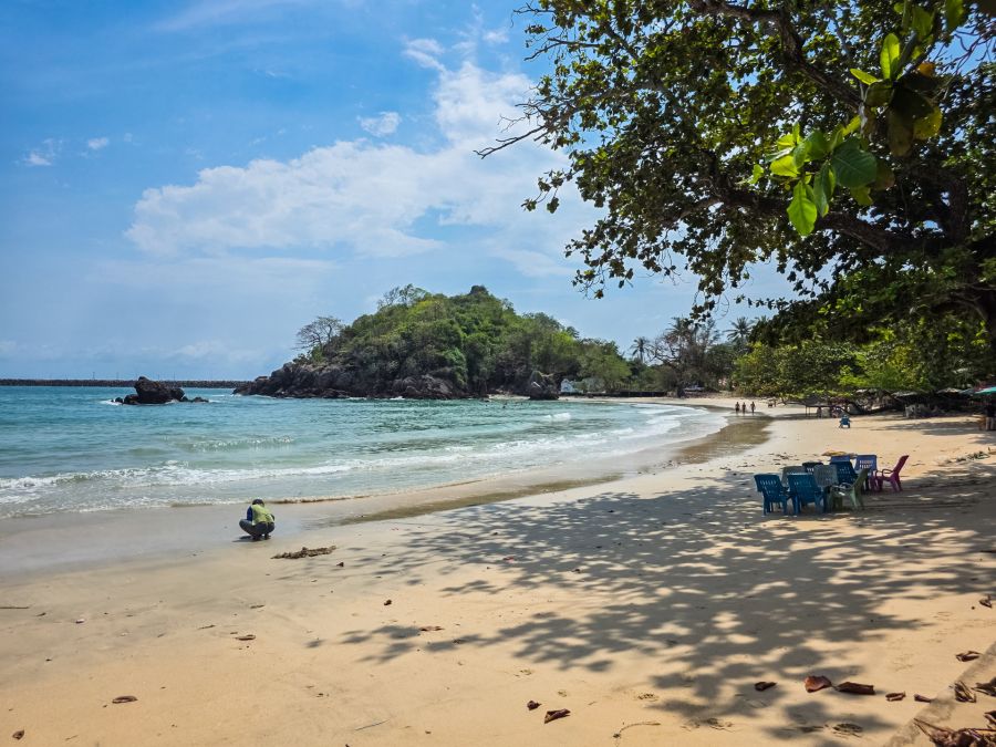 Tropical beach lined with trees and a rocky hill
