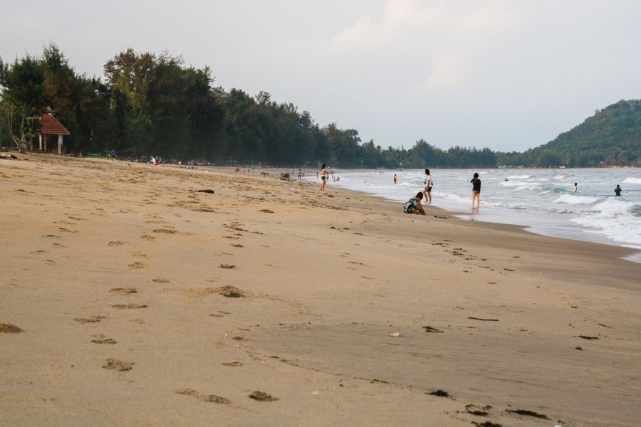 Sandy beach with bathers, waves and wooded hills