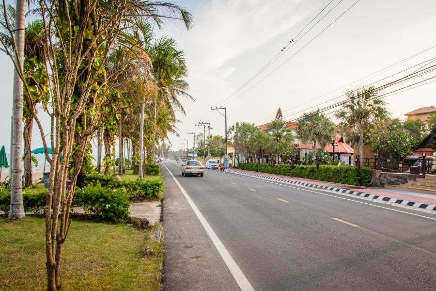 Coastal road lined with palm trees, cars and tropical shops