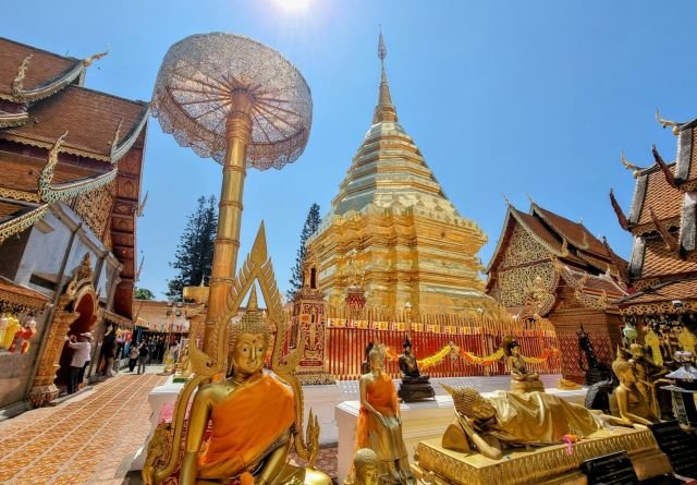 Wat Phra That Doi Suthep à Chiang Mai : chedi doré, statues bouddhiques et parasol ouvragé sous un grand ciel bleu, vue emblématique du temple.