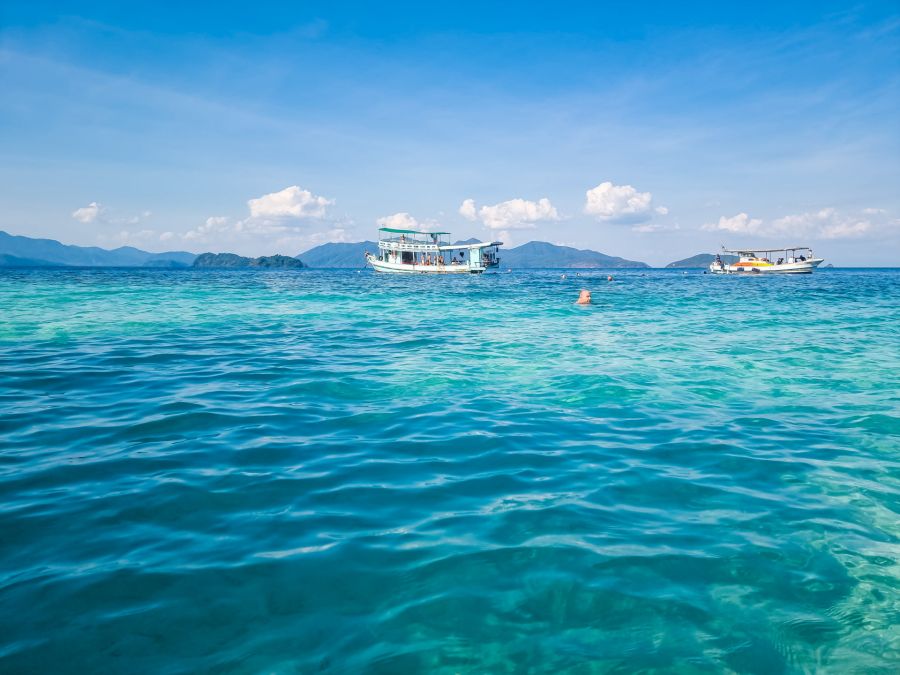Bateaux et nageur sur mer turquoise devant des montagnes