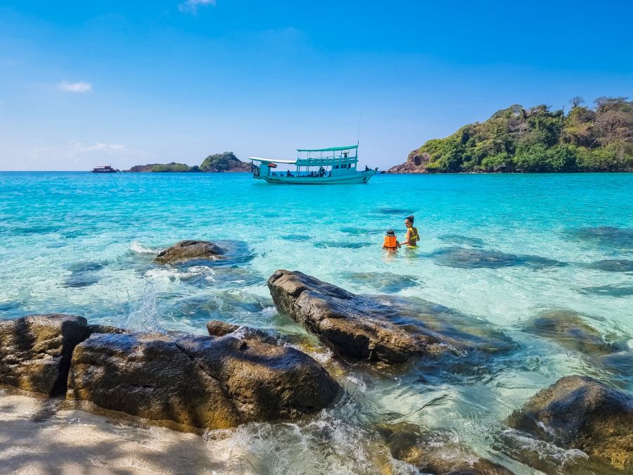 Bateau et baigneurs dans une mer turquoise bordée de rochers