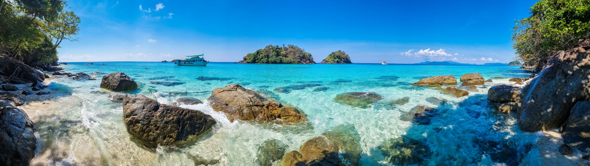 Plage tropicale rocheuse, eau turquoise, îlots et bateaux