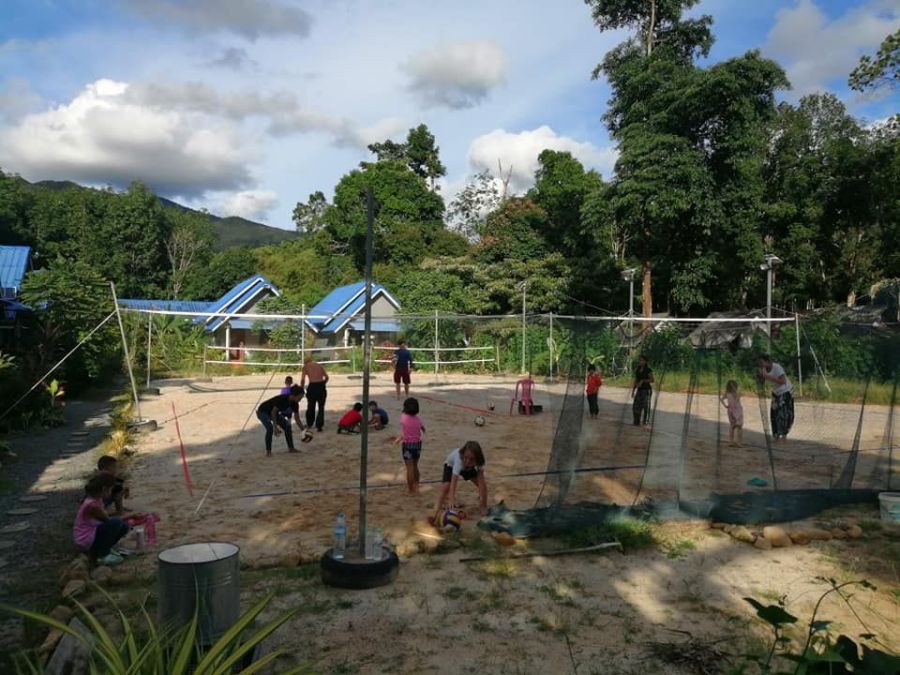 Enfants jouant au volleyball sur un terrain sablonneux entouré d’arbres