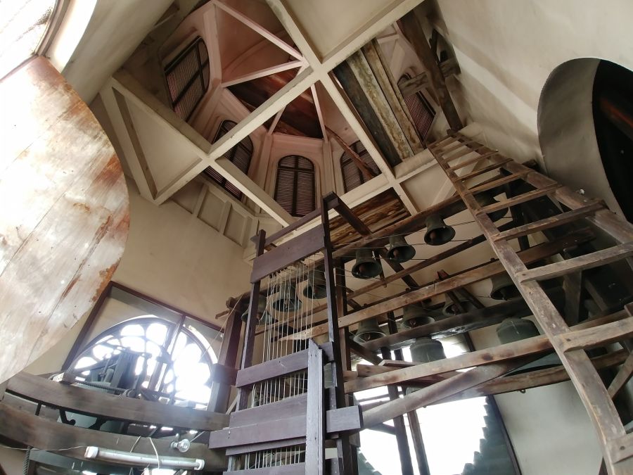 Intérieur d’un clocher avec cloches, charpente et échelles en bois
