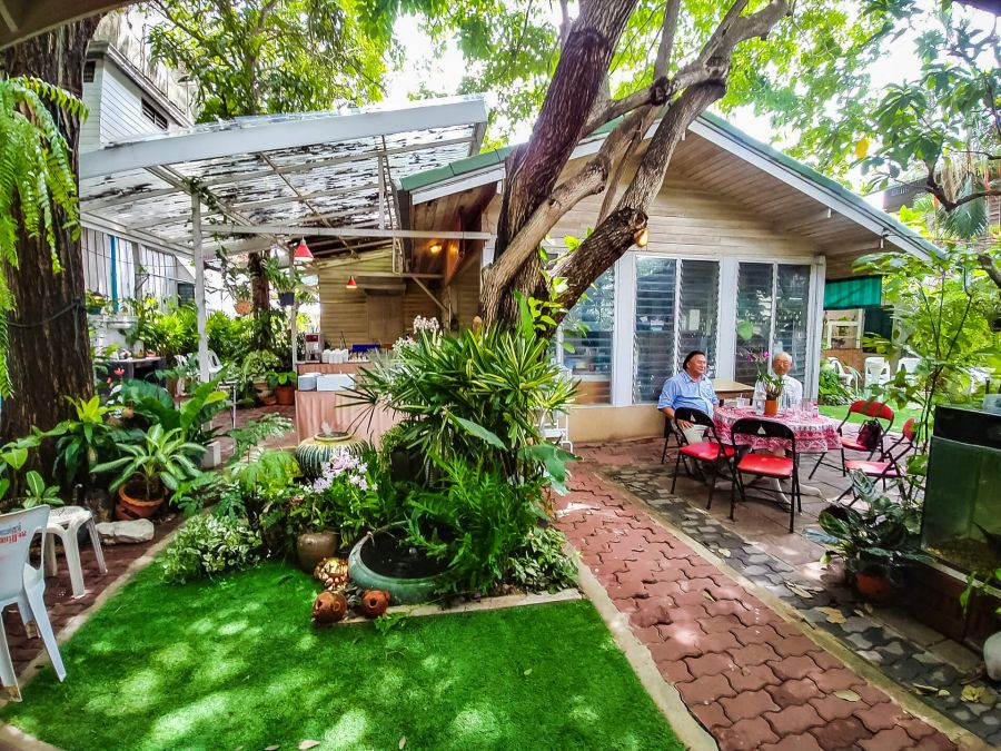 Terrasse verdoyante avec table, deux personnes et grand arbre