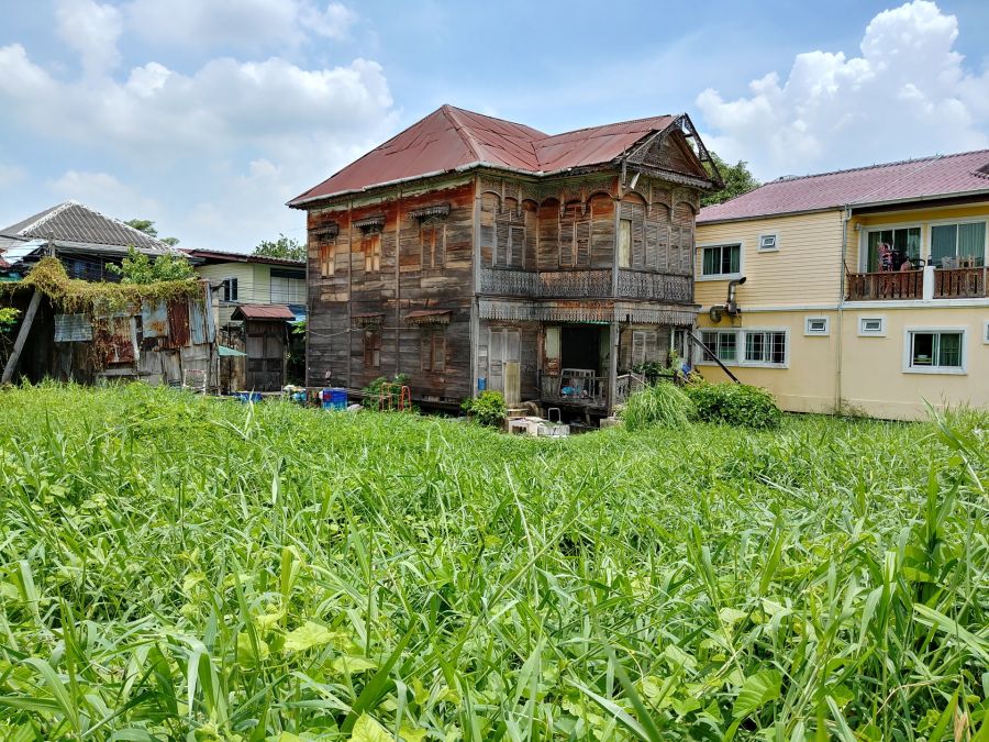 Maison traditionnelle en bois derrière un terrain envahi d’herbes