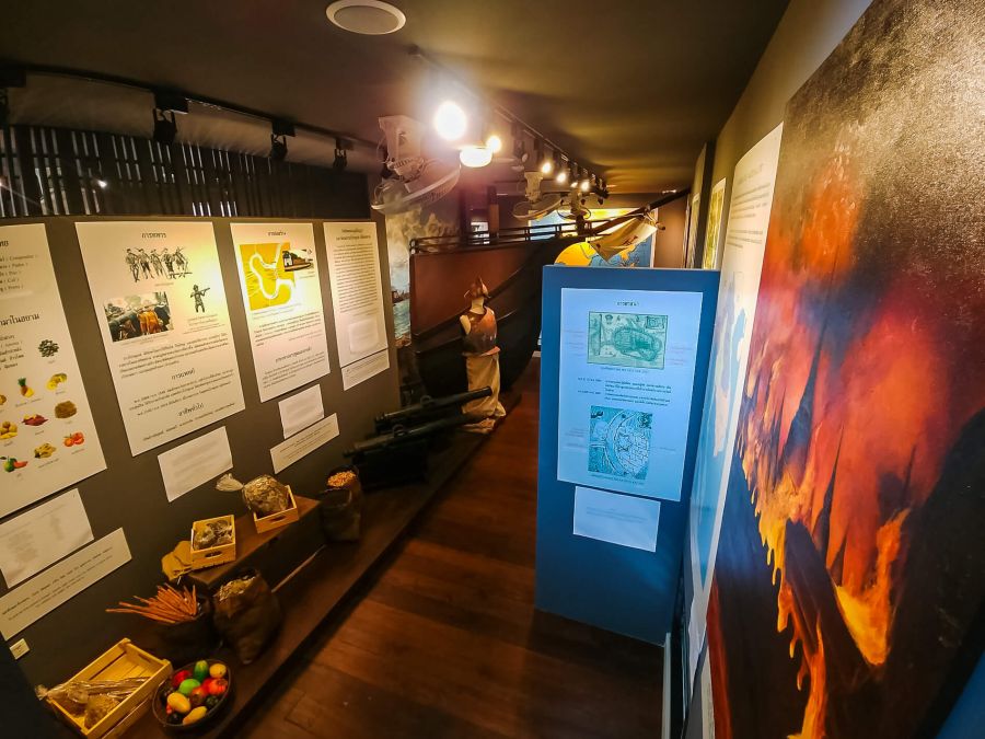 Exposition muséale avec panneaux explicatifs, objets et fresque colorée