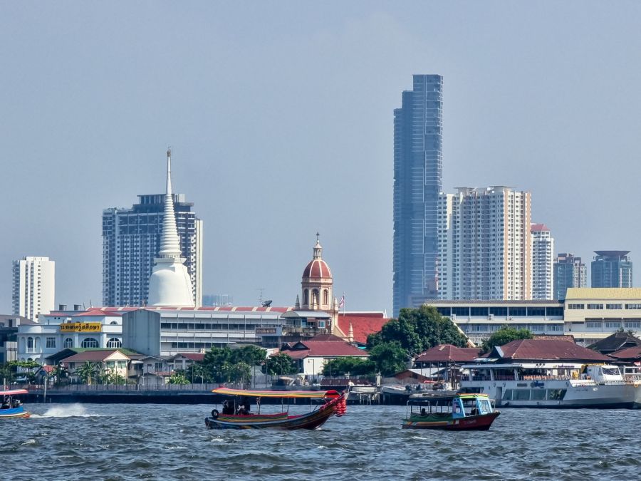 Bateaux sur le fleuve devant temples et gratte-ciel à Bangkok