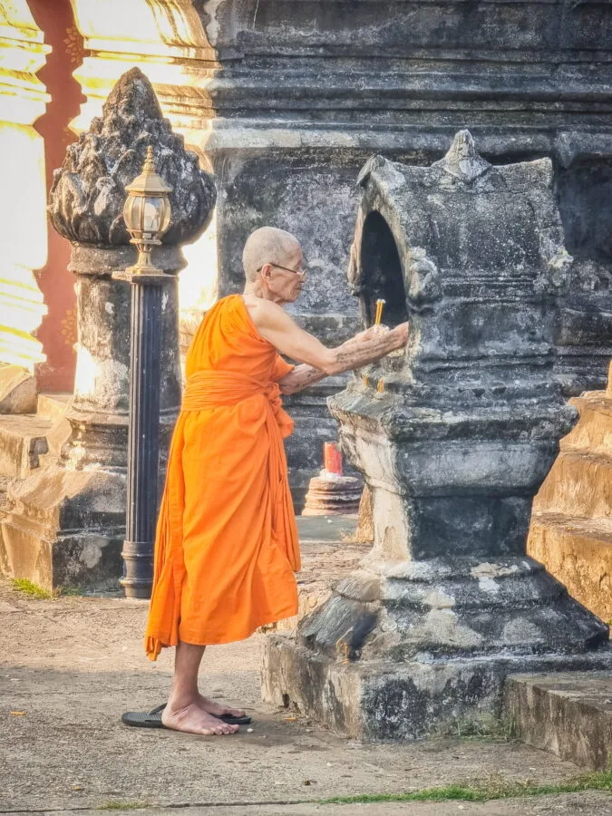 monk lights candle Wat Mai Suwannaphumaham Luang Prabang
