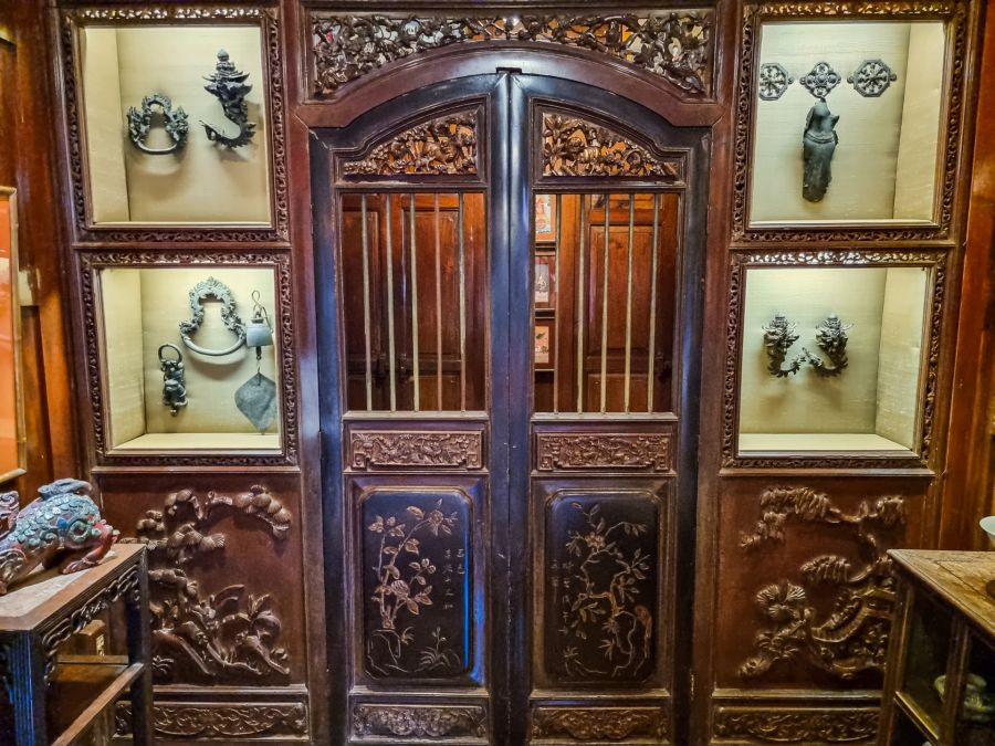 Porte chinoise sculptée entourée de vitrines d’objets anciens