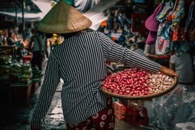 habitante portant un panier échalotes et ail dans un marché au Vietnam