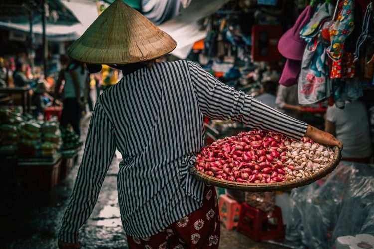 habitante portant un panier échalotes et ail dans un marché au Vietnam