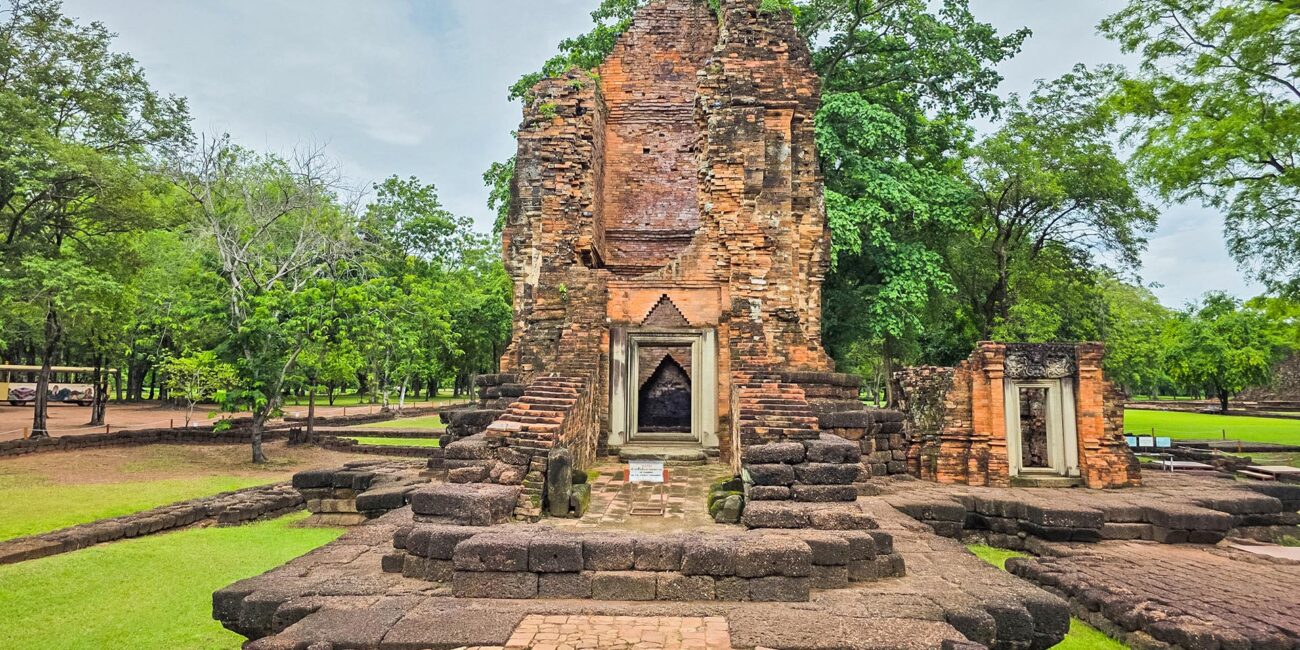 Khmer prang of Si Thep, brick road in the foreground, green park.