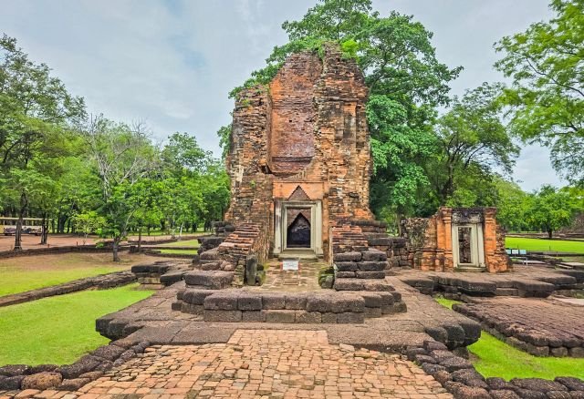 Prang khmer de Si Thep, chaussée en briques au premier plan, parc verdoyant.