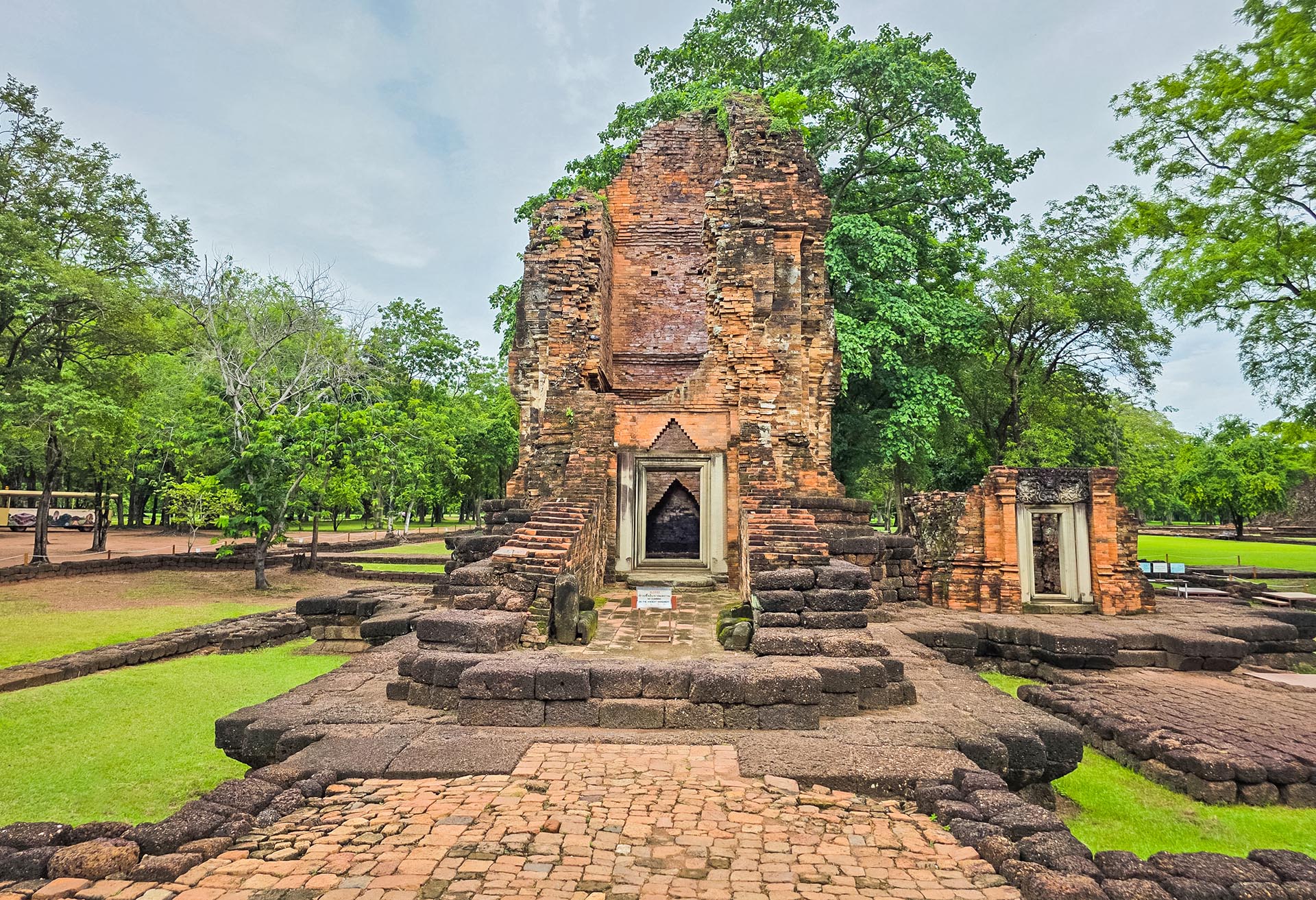 Khmer prang of Si Thep, brick road in the foreground, green park.